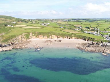 An aerial view of a beach with rocky shores and green fields with houses in the background at Bwthyn Y Bae Lodge in Church Bay near Llanfaethlu