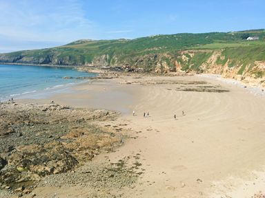 A sandy beach with rocky areas and people walking near cliffs at Bwthyn Y Bae Lodge in Church Bay near Llanfaethlu