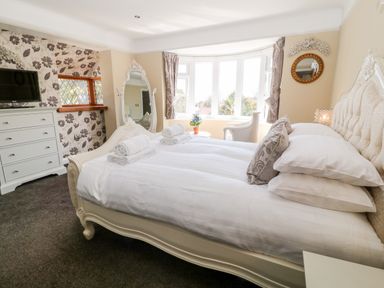 A bedroom with a large bed folded towels on it a dresser a wall mirror and a bay window at Harbour Lights in Torquay