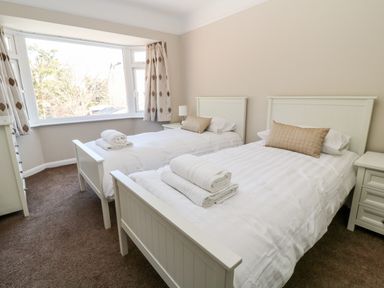 A bedroom with two single beds with folded towels on white bedding and a large window with patterned curtains at Harbour Lights in Torquay
