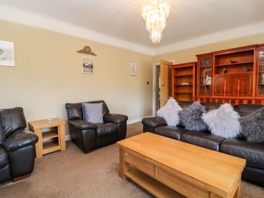 A living room with leather armchairs wooden coffee table and a wooden cabinet at Harbour Lights in Torquay