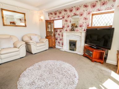 A living room with beige armchairs a fireplace a television on a wooden stand and floral wallpaper at Harbour Lights in Torquay