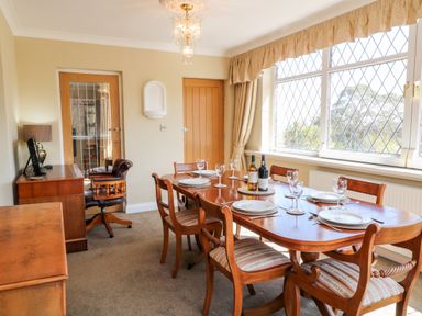 A dining room with a wooden table set with plates and glasses and wooden chairs near a large window at Harbour Lights in Torquay