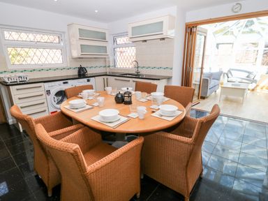 A kitchen with a round dining table set for six and wicker chairs next to a conservatory at Harbour Lights in Torquay