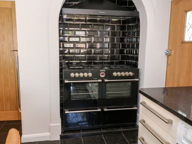 A black stove with multiple burners and ovens set into a tiled alcove with black glossy subway tiles in a kitchen at Harbour Lights in Torquay