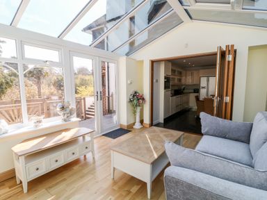 A sunroom with glass ceiling and walls overlooking a patio next to a kitchen with wooden folding doors at Harbour Lights in Torquay