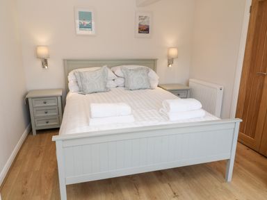 A bedroom with a double bed, bedside tables, lamps, two framed pictures on the wall and folded towels on the bed at Harbour Lights in Torquay