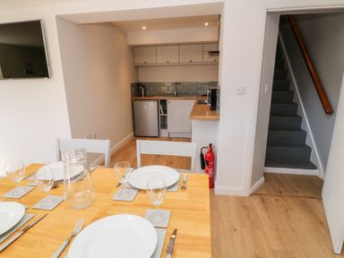 A dining table set with plates glasses and cutlery in a kitchen with wooden floors stairs and a fire extinguisher at Harbour Lights in Torquay