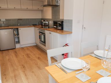 A kitchen with wooden countertops gray cabinets a stainless steel oven microwave toaster and a dining table with place settings and chairs at Harbour Lights in Torquay