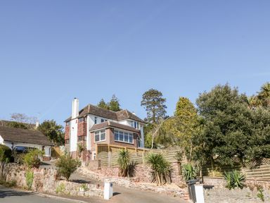 A two-story house with a driveway and garden surrounded by a stone wall and wooden fence at Harbour Lights in Torquay