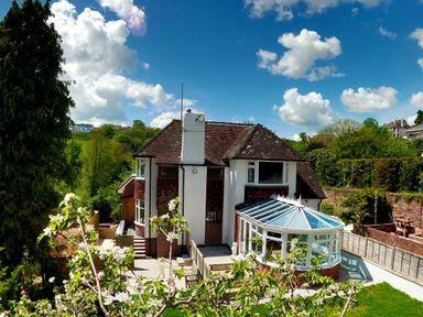 A house with a conservatory and garden surrounded by trees and fields at Harbour Lights in Torquay