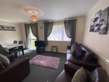 A living room with two brown sofas, a small table with a TV, grey curtains on windows, and a dining table with chairs at Lands End in Liskeard near St Cleer