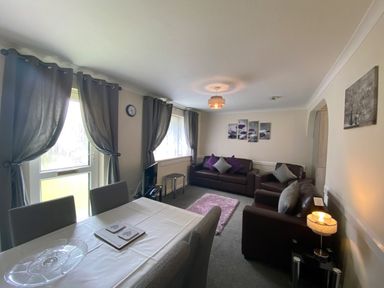 A living room with sofas dining table a carpet and curtains at Lands End in Liskeard near St Cleer
