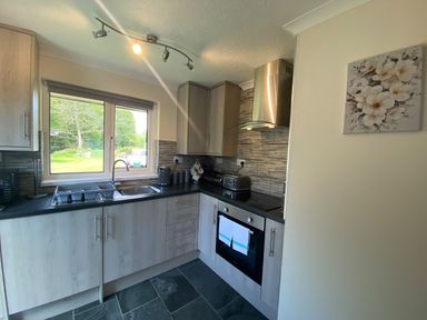 A kitchen with grey cabinets a window above a sink and an oven with a hood at Lands End Liskeard near St Cleer