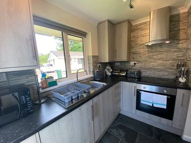 A kitchen with wooden cabinets a black countertop a microwave a dish rack above the sink and an oven with towels at Lands End in Liskeard near St Cleer