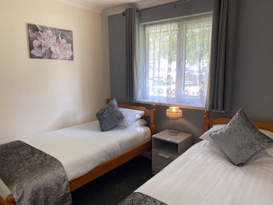 A bedroom with two single beds a window with curtains a nightstand and a lamp at Lands End in Liskeard near St Cleer