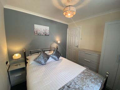 A bedroom with a double bed two pillows a bedside table with lamp a chest of drawers and a wardrobe at Lands End in Liskeard near St Cleer