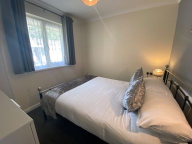 A bedroom with a bed pillows a window with curtains and a bedside lamp at Lands End in Liskeard near St Cleer
