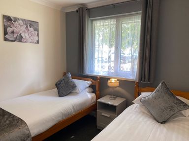 A bedroom with two single beds a window with curtains and a nightstand with a lamp at Lands End in Liskeard near St Cleer