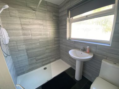 A bathroom with a walk-in shower a pedestal sink with hand soap a toilet and a window with a blind at Lands End in Liskeard near St Cleer