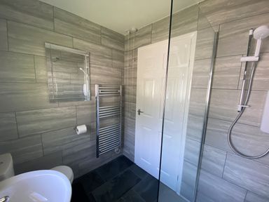 A bathroom with a sink, toilet, wall mirror, towel radiator, showerhead, and a white door at Lands End in Liskeard near St Cleer