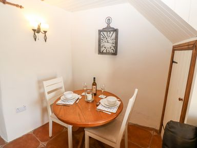 A small dining area with a round wooden table set for two with white chairs and a wall clock at Bwthyn Siop Pencaerau in Rhiw near Aberdaron
