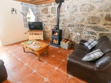 A living room with a wood burning stove a brown leather sofa and a wooden coffee table at Bwthyn Siop Pencaerau in Rhiw near Aberdaron
