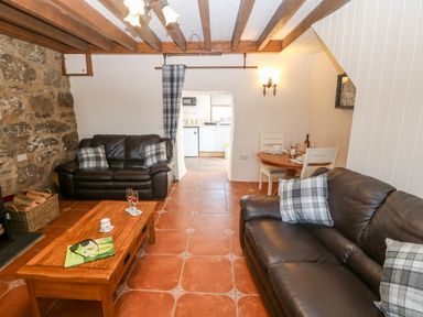 A sitting room with two leather sofas a wooden coffee table and a small dining area with a round table at Bwthyn Siop Pencaerau in Rhiw near Aberdaron
