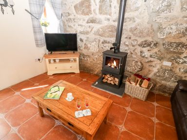 A living room with a wood burning stove and tv on a stand at Bwthyn Siop Pencaerau in Rhiw near Aberdaron