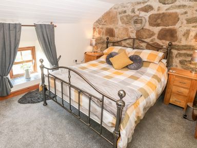 A bedroom with a metal bed frame a checkered bedspread and wooden nightstands with lamps at Bwthyn Siop Pencaerau Rhiw near Aberdaron