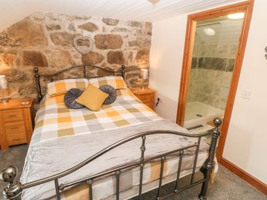 A bedroom with a metal bed frame and checkered bedding with side tables and lamps and an en suite shower at Bwthyn Siop Pencaerau in Rhiw near Aberdaron