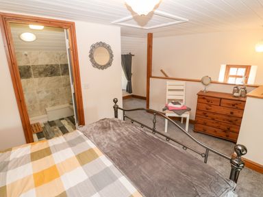 A bedroom with a metal bed frame a wooden dresser a white chair with folded towels and an ensuite bathroom at Bwthyn Siop Pencaerau in Rhiw near Aberdaron