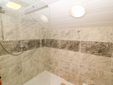 A tiled shower area with a glass partition and a ceiling light at Bwthyn Siop Pencaerau in Rhiw near Aberdaron