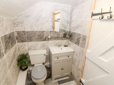 A small bathroom with a toilet a sink with cabinet a mirror and hooks on the door at Bwthyn Siop Pencaerau in Rhiw near Aberdaron