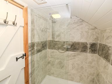 A tiled shower area with a glass partition and a white wooden door with hooks at Bwthyn Siop Pencaerau in Rhiw near Aberdaron