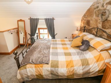 A bedroom with a bed with checkered bedding gray curtains and a standing mirror at Bwthyn Siop Pencaerau in Rhiw near Aberdaron