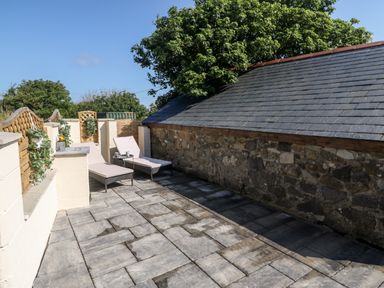 An outdoor patio area with two lounge chairs and a small table next to a stone wall at Bwthyn Siop Pencaerau in Rhiw near Aberdaron