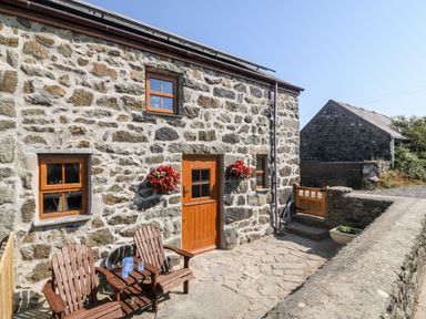 Stone cottage exterior with wooden door two wooden chairs and hanging flower baskets at Bwthyn Siop Pencaerau in Rhiw near Aberdaron