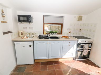 A kitchen with a microwave a small fridge a kettle a sink an oven and a window at Bwthyn Siop Pencaerau Rhiw near Aberdaron