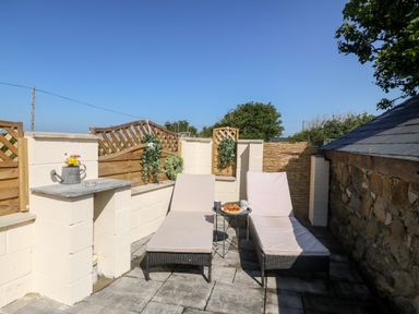 An outdoor patio area with two lounge chairs a small table with croissants and cups and a watering can with flowers at Bwthyn Siop Pencaerau in Rhiw near Aberdaron