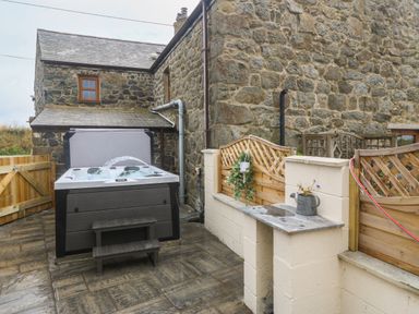 A stone building exterior with a hot tub and wooden fencing at Bwthyn Siop Pencaerau in Rhiw near Aberdaron