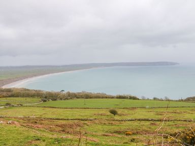 A coastal landscape with green fields and stone walls by the sea at Bwthyn Siop Pencaerau in Rhiw near Aberdaron