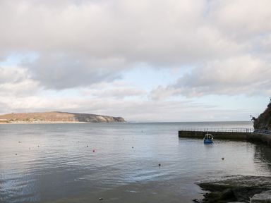 A coastal scene with a small boat near a pier and rocky shoreline at Bwthyn Siop Pencaerau in Rhiw near Aberdaron