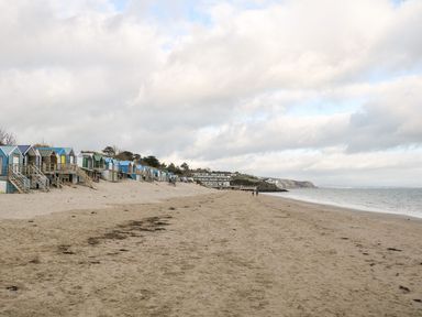 A sandy beach with small colorful beach huts along the left side and the sea on the right at Bwthyn Siop Pencaerau Rhiw near Aberdaron
