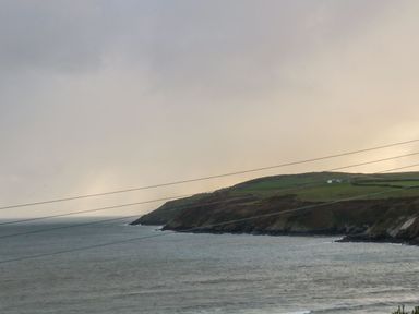 A coastal landscape with cliffs and green fields beside the sea at Bwthyn Siop Pencaerau in Rhiw near Aberdaron