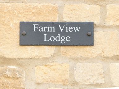 A black rectangular sign with white text mounted on a beige stone wall reading Farm View Lodge