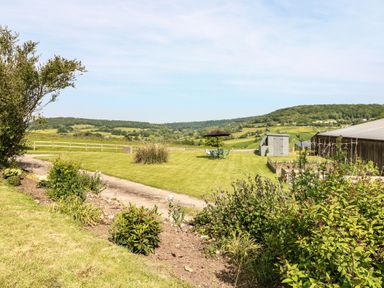 A garden with a patio table and umbrella shed and plants with hills in the background at Farm View Lodge in Painswick