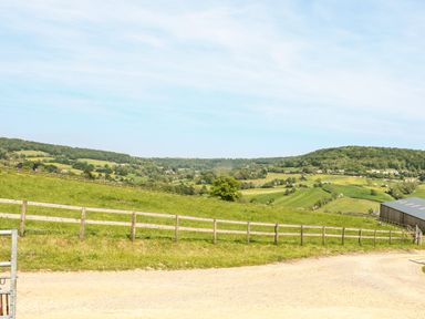 A rural landscape with green fields hills a wooden fence and a metal barn at Farm View Lodge in Painswick