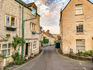 A narrow street with stone houses on both sides and flowers growing by the doors at Farm View Lodge in Painswick
