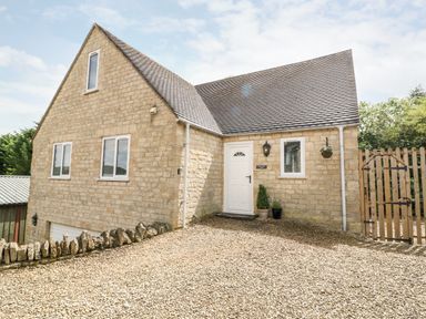 A stone house with a gravel driveway a white door and windows and a wooden gate at Farm View Lodge in Painswick